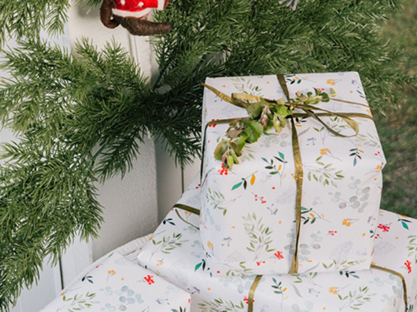 A selection of Christmas presents in white and botanical wrapping paper sitting under a Christmas tree. 