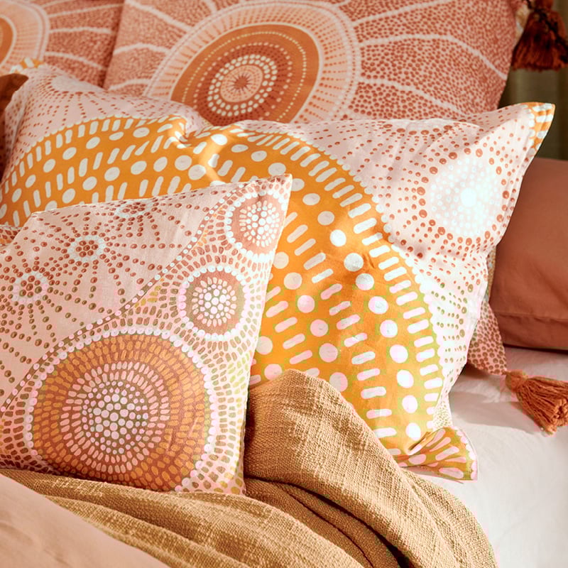 Close-up shot of the beautiful patterns on the pillowcases available in the collection, showcasing the Indigenous artwork of Brad Turner with vibrant orange against pastel hues of earth, pink and yellow. 