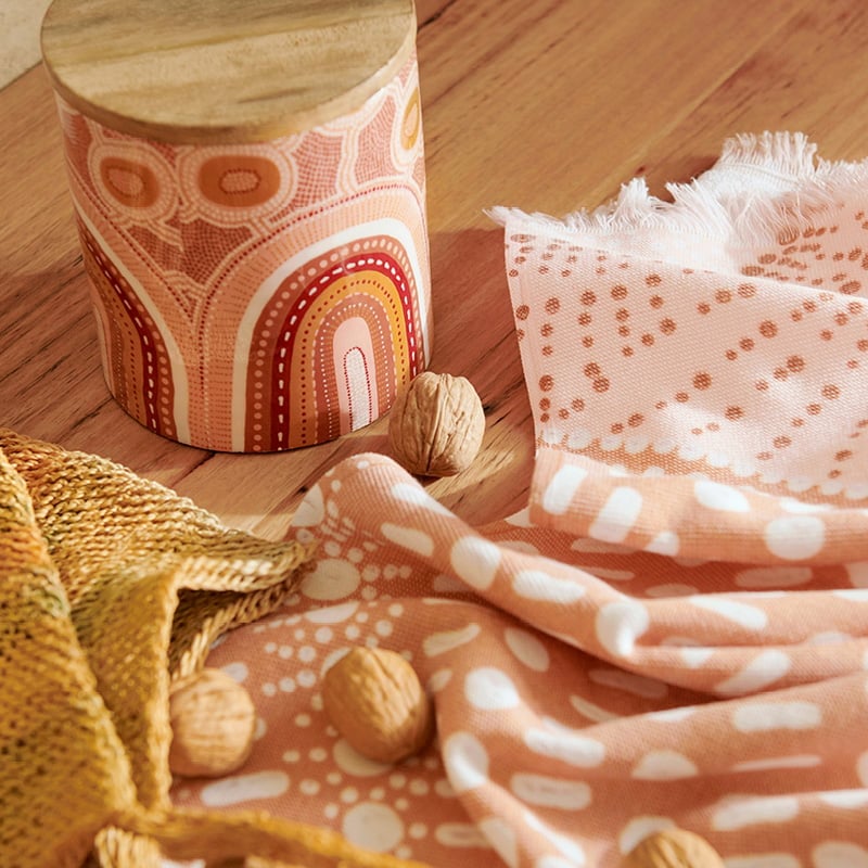 Wooden container with Indigenous artwork in reds, pink, orange and earth, styled on a timber table.