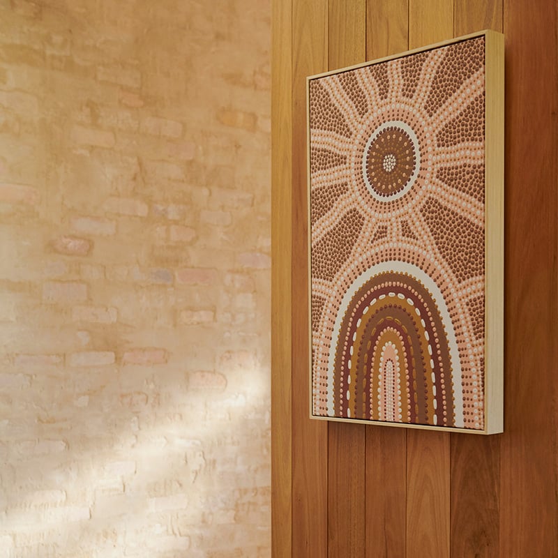 Brad Turner artwork hangs against wooden panelled wall in hues of brown and pink, in the dotted pattern showcasing a shining sun.
