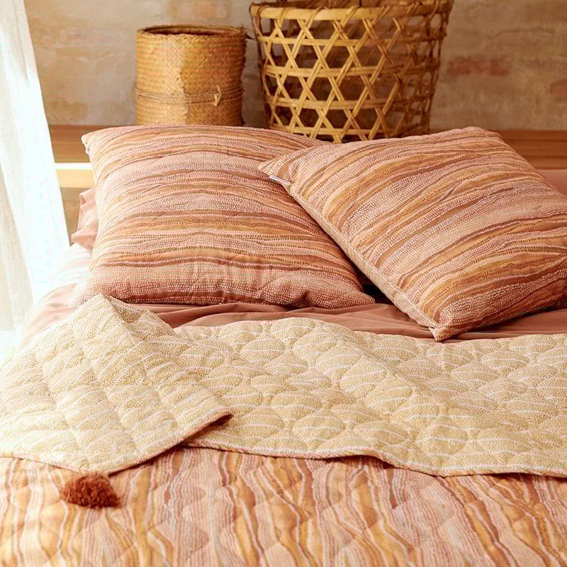 Two cushions styled on a bed to accompany the coverlet, in tones of earth and lighter shades of pink, yellow and orange.