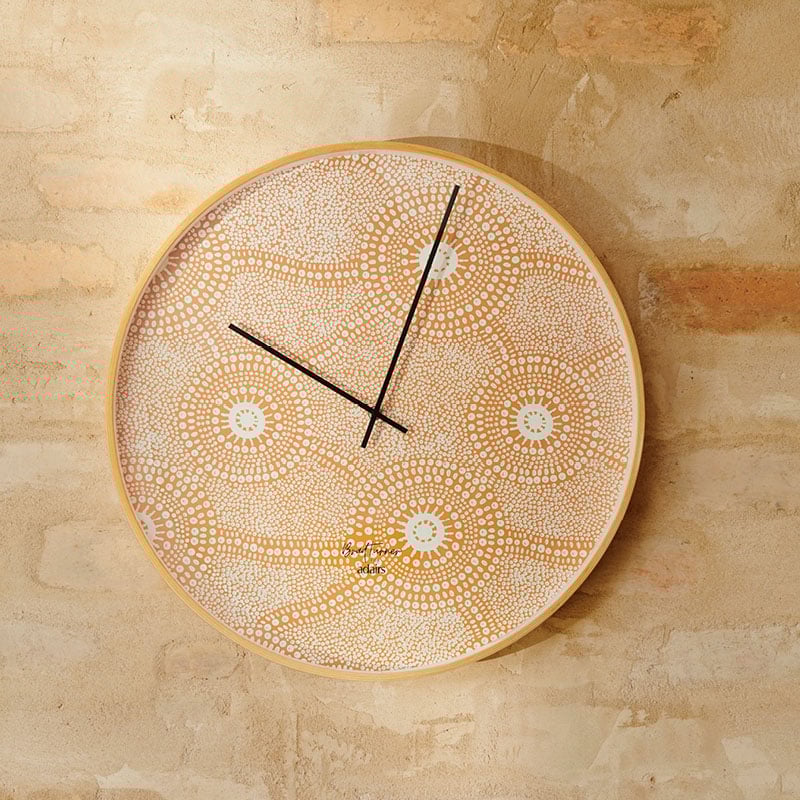 Circular analog wall clock against an earthy toned brick wall, with defined black hands contrasting against the vibrant orange dotted design. 