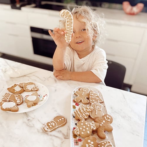 Toddler at kitchen bench with plate of Christmas gingerbread cookies. 
