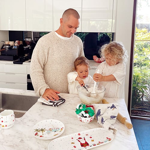 Father with two young children baking Christmas gingerbread cookies at kitchen bench.