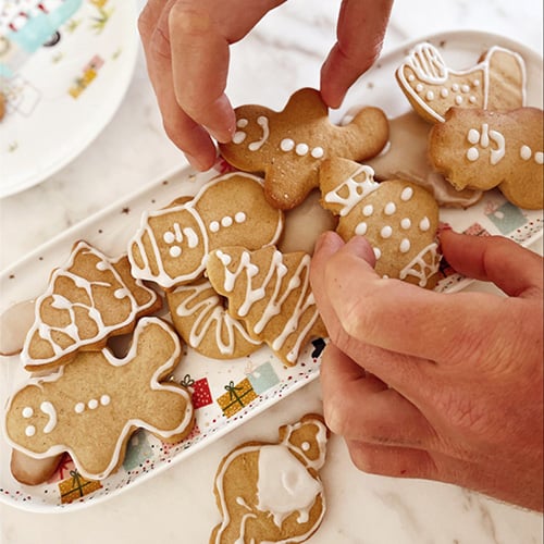 Hands arranging Christmas gingerbread cookies onto a Christmas plate