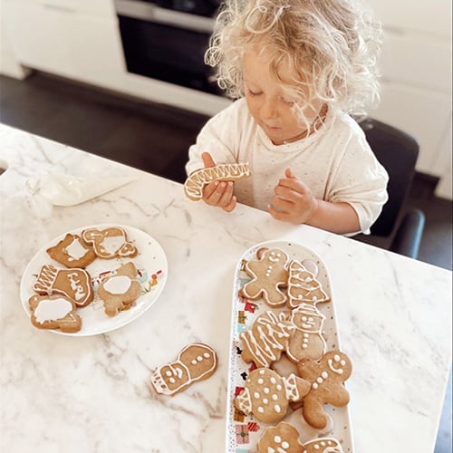 Toddler at kitchen bench eats a Christmas gingerbread cookie.