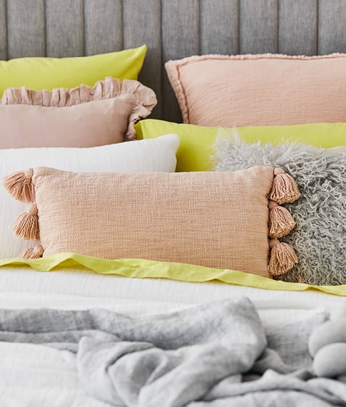 Various pillows with yellow, pink and grey tones placed on the bed