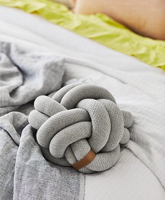 Grey unique cushion placed on the bed, with white and grey sheets