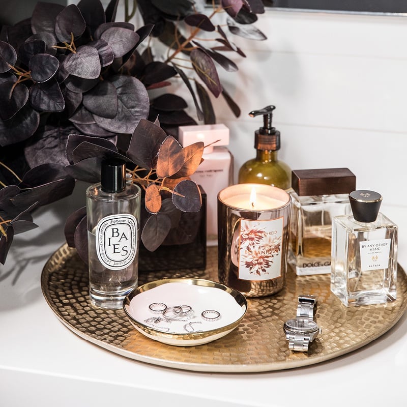 Vanity collection of perfume, lit candle and jewellery. 