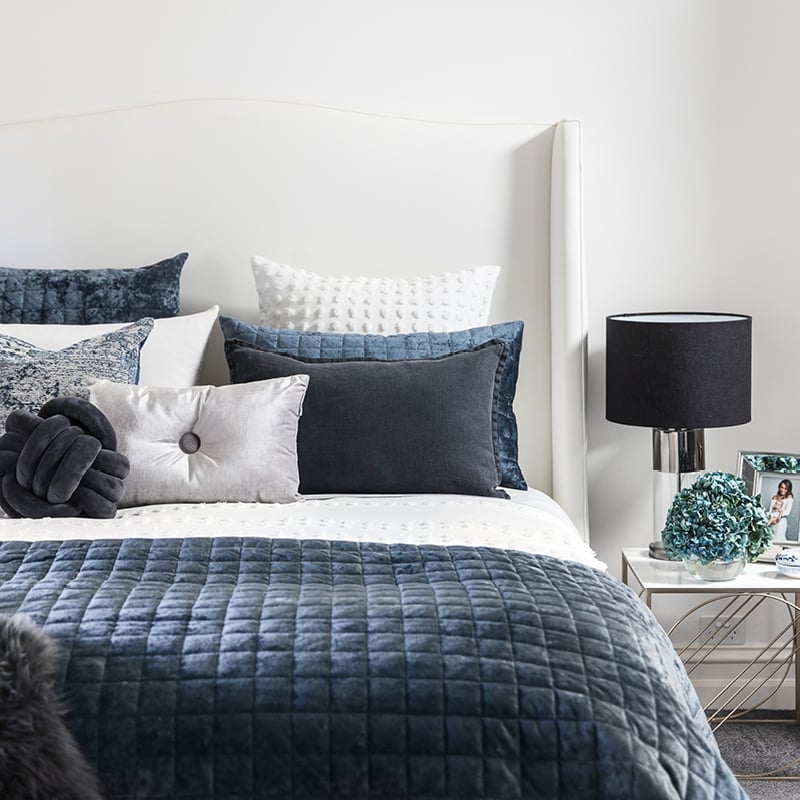 Luxurious navy blue coverlet and matching pillowcases, styled against a white textured quilt cover and decorative cushions in velvet silver and vintage blue.
