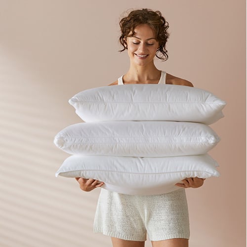 Woman/man standing holding three supportive pillows stacked on top of each other. 