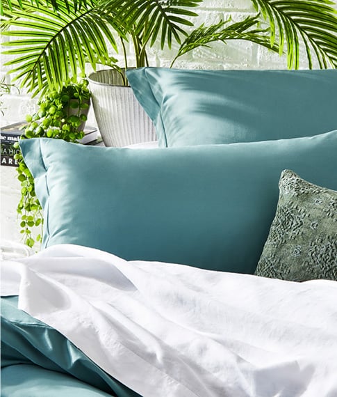 Close-up of Bamboo Cotton Quilt Cover and matching pillowcases styled with white sheets and plants behind. 