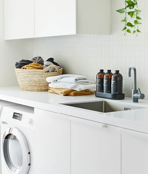 Laundry with white finishes, styled with Navara Bamboo Towels both in a basket and stack, next to a selection of Aroma Wash. 