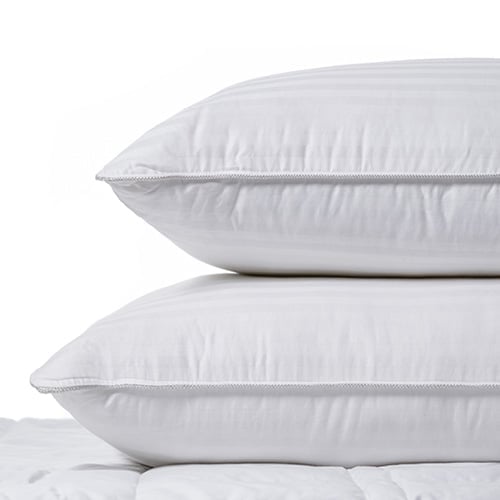Two feather and down pillows stacked on top of each other sitting on a mattress. 