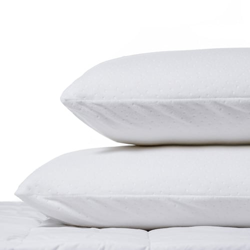 Two natural latex pillows stacked on top of each other sitting on a mattress. 