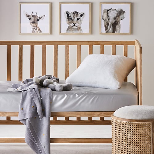 A baby’s rattan cot styled with silver silk bottom sheet and on top sits a soft cushion, throw and plush toy. 