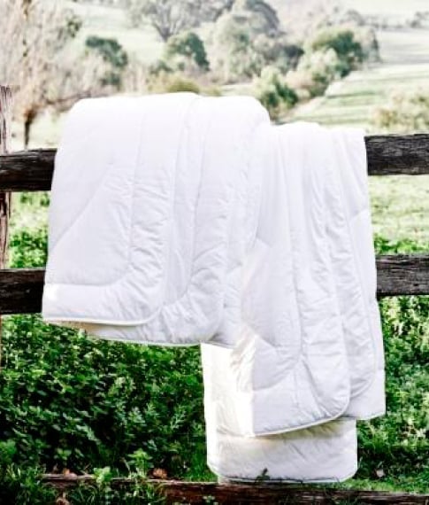 Outdoor setting white mattress protector placed hanging of a wooden fence, with a green nature background