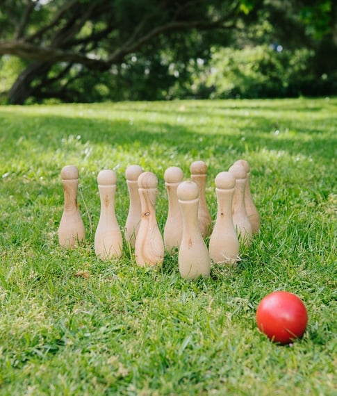 A backyard with lush green grass and a set of wooden bowling pins lined up ready to play.