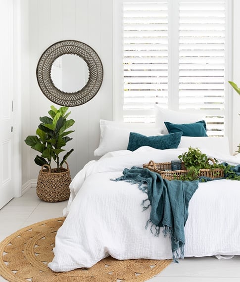 Bed with classic white bedlinen styled back with navy accessories, rattan tray, basket with plant and matching mirror.