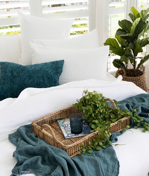 Close-up of tray styled on top of a white bedlinen and navy linen throw with a pot plant in the background.