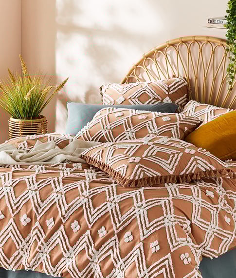 Terracotta bedlinen with textured tufting in diamond patterns on a bed with a rattan bedhead and colourful accessories.