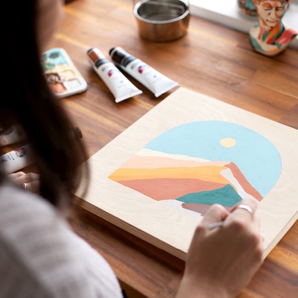 Claudia is painting a landscape scene in her sketchbook. The photo is taken over Claudia’s shoulder.