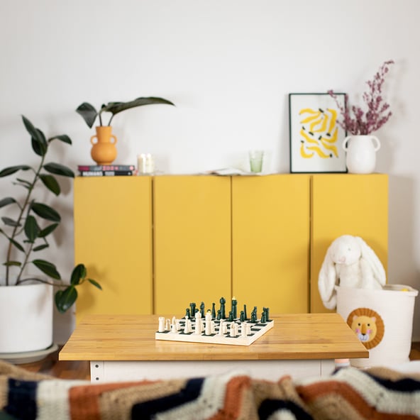 A front-on shot of a yellow sideboard, with a coffee table and couch in the foreground. There are plants and home décor pieces throughout the scene.