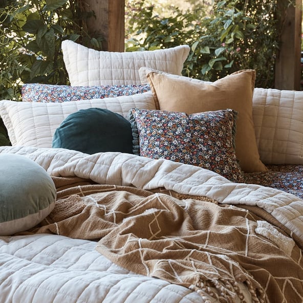 A close up, angled view of floral, velvet and quilted cushions arranged on a bed