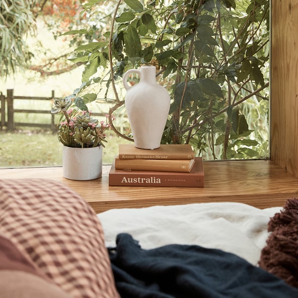 A front view looking out a window to a country scene with a pile of books and two white vases sitting on the window sill.