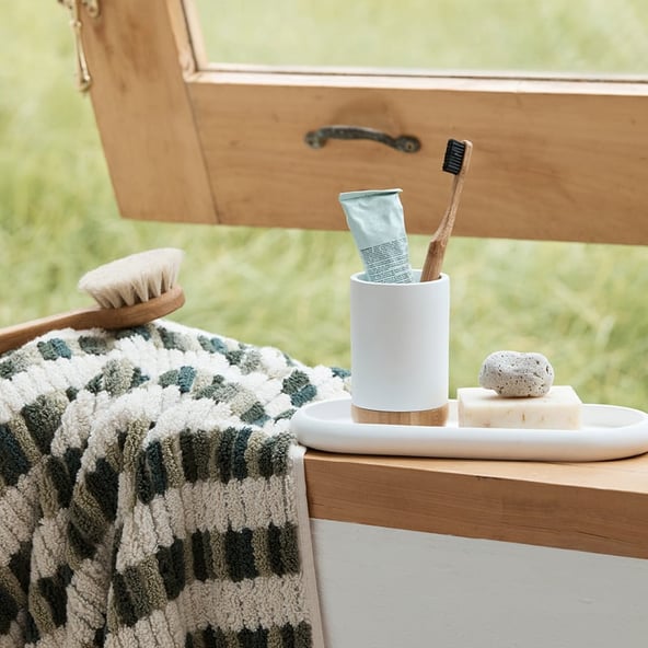 A green patterned towel and a small marble tray filled bathroom accessories sits on a window sill in front of the slightly ajar window.
