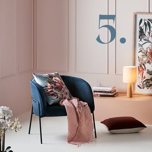 Corner of bedroom with navy chair, styled with printed floral cushion, throw and printed wall art in the background. 