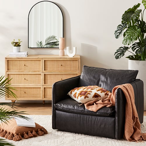 Atticus Leather Armchair in black styled with warm orange accessories, and behind sits pot plants and an Anjuna Chest of Drawers. 
