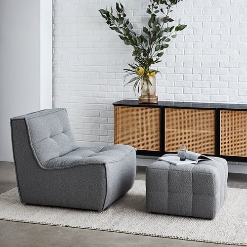 Otis Lounge Chair in dark grey with matching footrest and behind is a Boden Black & Natural 3 Door Sideboard with vase on top. 