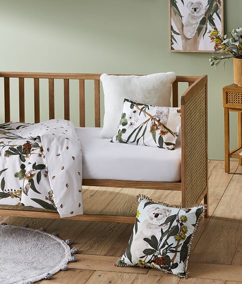 Arden Natural Rattan Nursery Cot with botanical and white matching bedlinen, and a Grey Pom Pom Rug. 