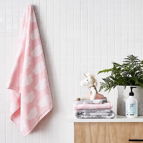 Baby cloud pink bath towel hanging in bathroom next to stack of matching towels, unicorn plush toy and kids aroma wash.