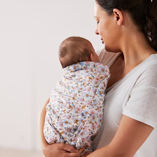 A mum cuddling a baby wrapped in a Fleur Harris Swaddle.