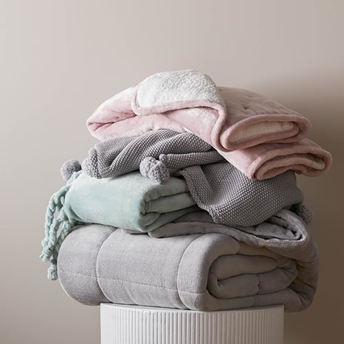 A stack of plush, fleecy, textured and tasselled baby blankets sitting on top of a round ribbed white table.