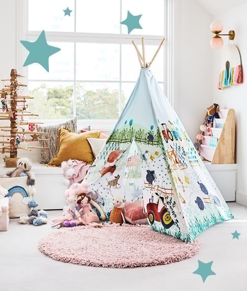 Kids playroom with bench seat in the background, a bookshelf and a tepee filled with plush toys in the foreground.