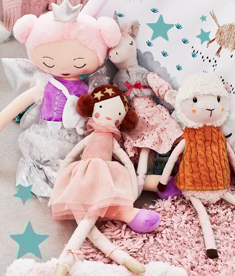 A collection of plush toys including a lamb, ballerina, horse, and fairy sitting together on top of a pink rug.