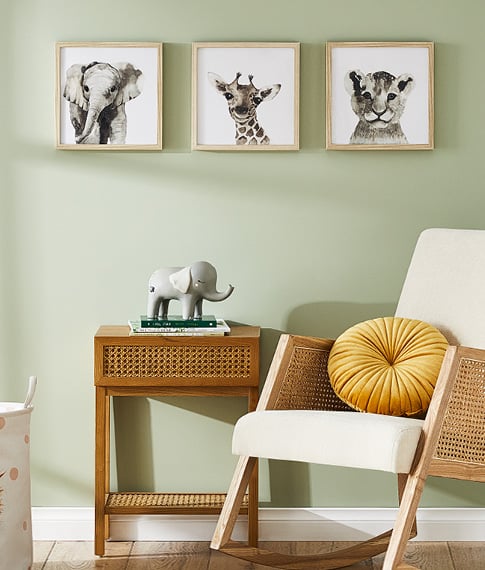 A rocking chair and side table next to a green wall featuring safari wall art with an elephant, giraffe and tiger.