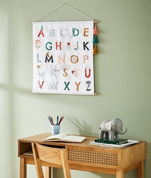 An alphabet wall art chart hanging above a children’s study desk.  