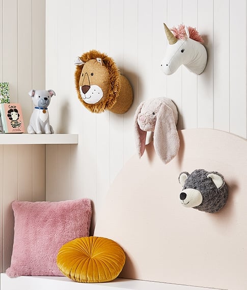 3D plush wall art including the face of a bunny, bear, lion and unicorn on a wall above a children’s reading nook. 