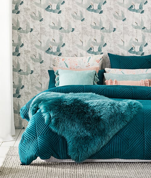 Bed with pastel teal soft and textured velvet quilt cover, various pillows floral prints in shades of pastel teal and pink displayed