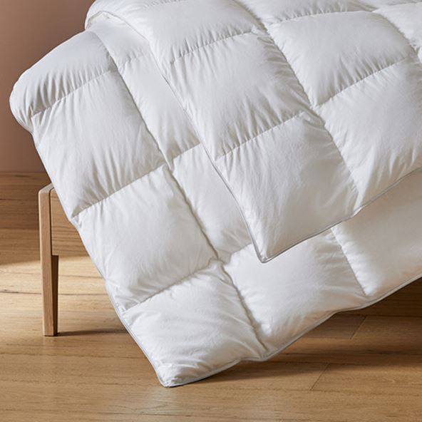 A plush down quilt hanging off the end of a wooden bed sitting on a hardwood floor. 