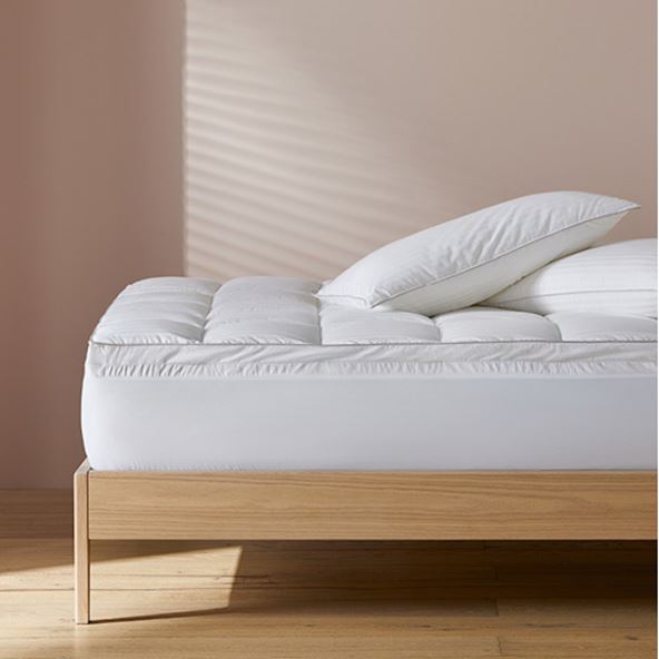 A mattress topper on a bed pushed against a wall with two pillows situated on top of the bed. 