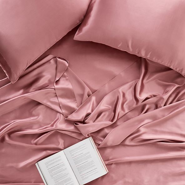 An aerial shot of an open book sitting on top of ruffled pink silk sheet.