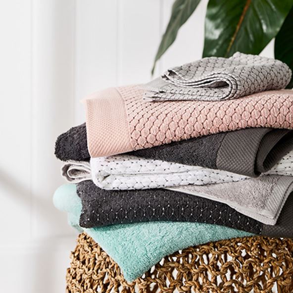 Stack of Bamboo Navara Towels including pink, coal, grey marle, white, and more – all on top of a rattan table. 