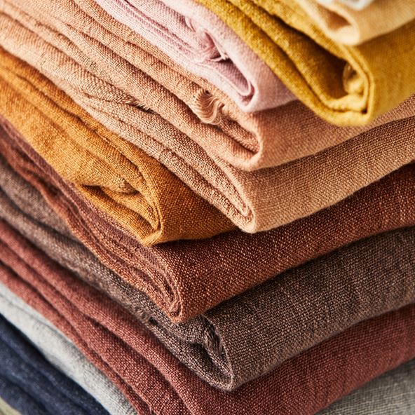 A close up shot of folded linen in multiple colours, showing the texture of the material.