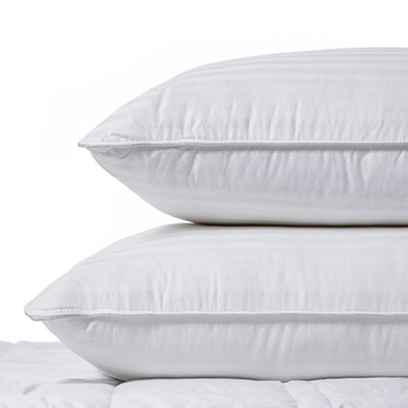 Two feather and down pillows stacked on top of each other sitting on a mattress. 