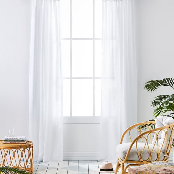 Living space scene of a window with white linen curtains displayed behind a bamboo coffee table and chair